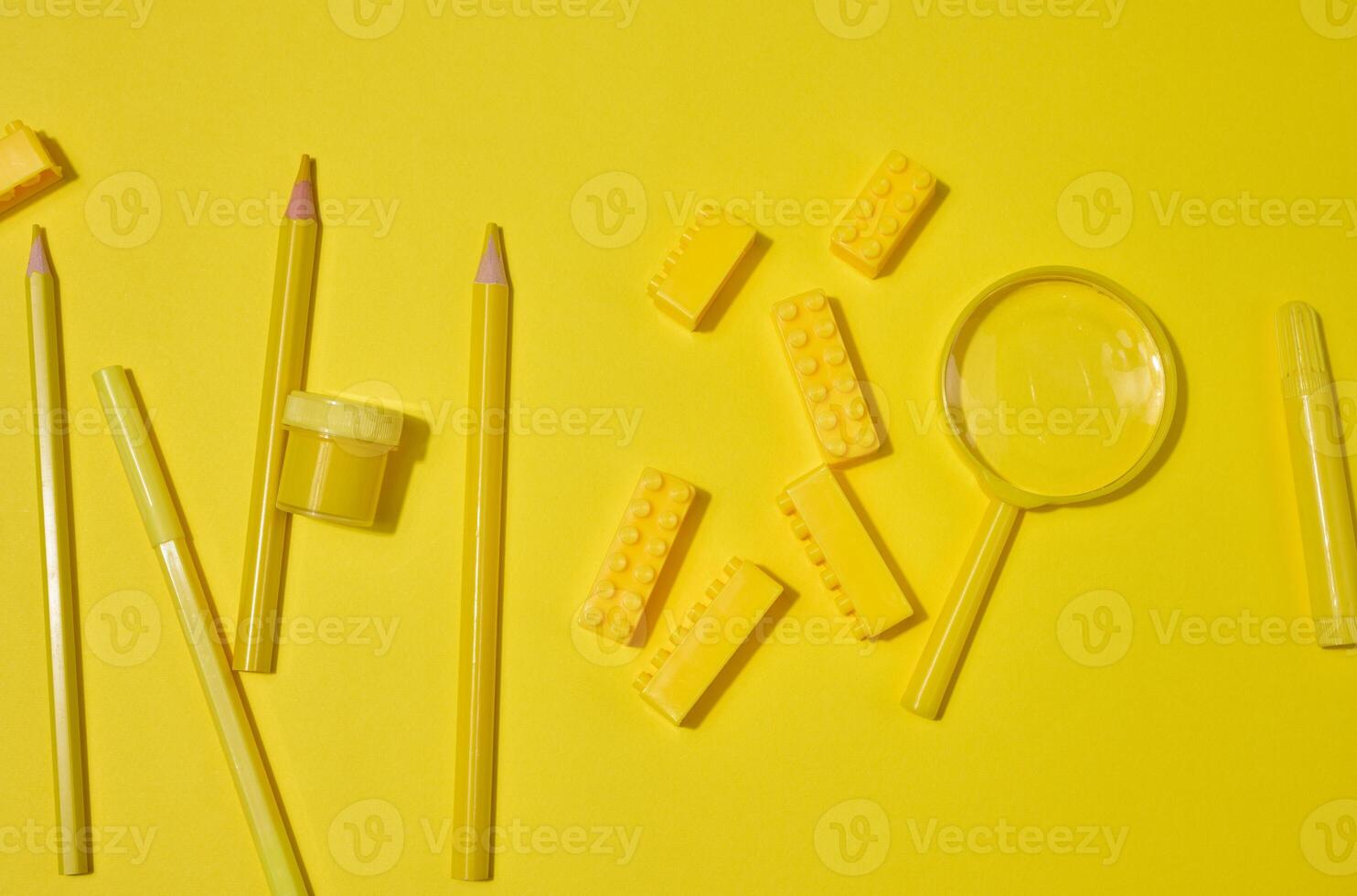 Collection of yellow stationery, building brick, and magnifying glass on a yellow background. Pencil, marker, jar included. Creative or learning concept. photo