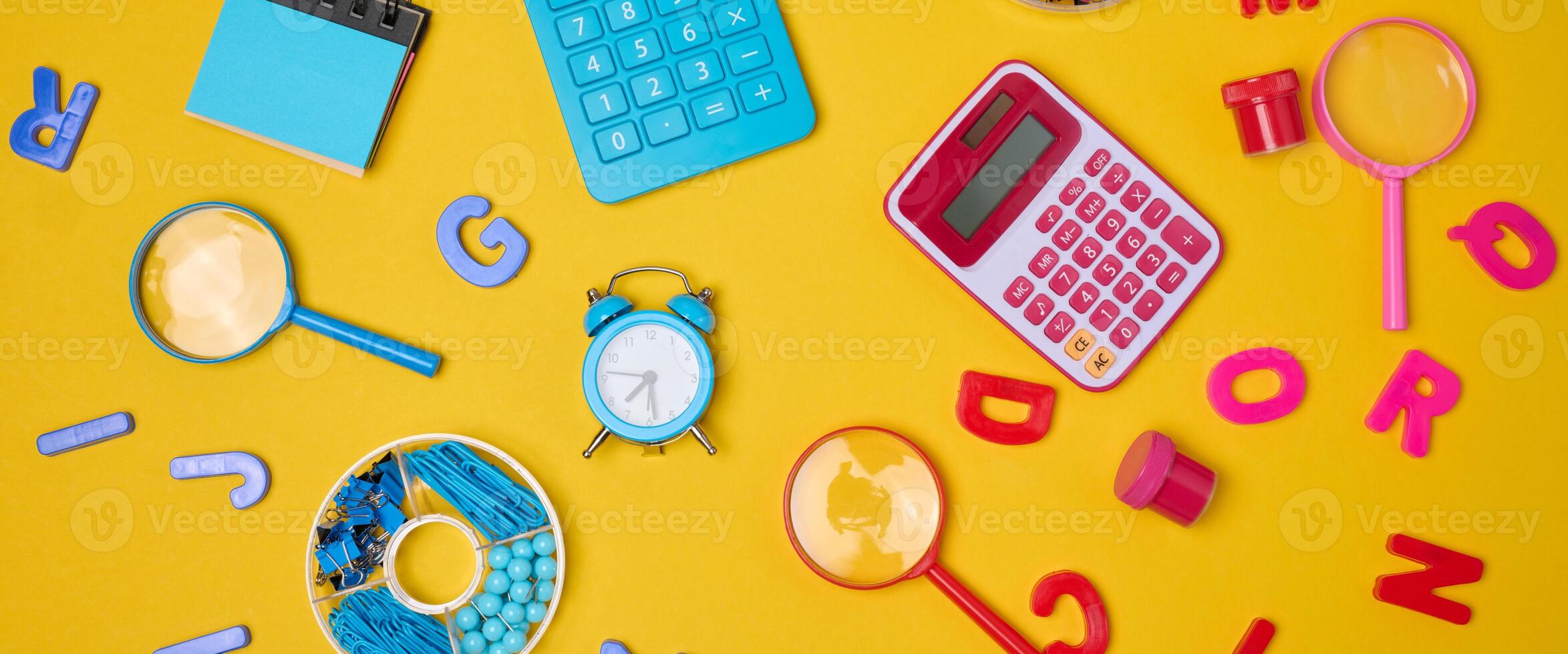 Colorful school supplies, learning items calculators, letters, tools, and stationery scattered on a vibrant yellow background. photo