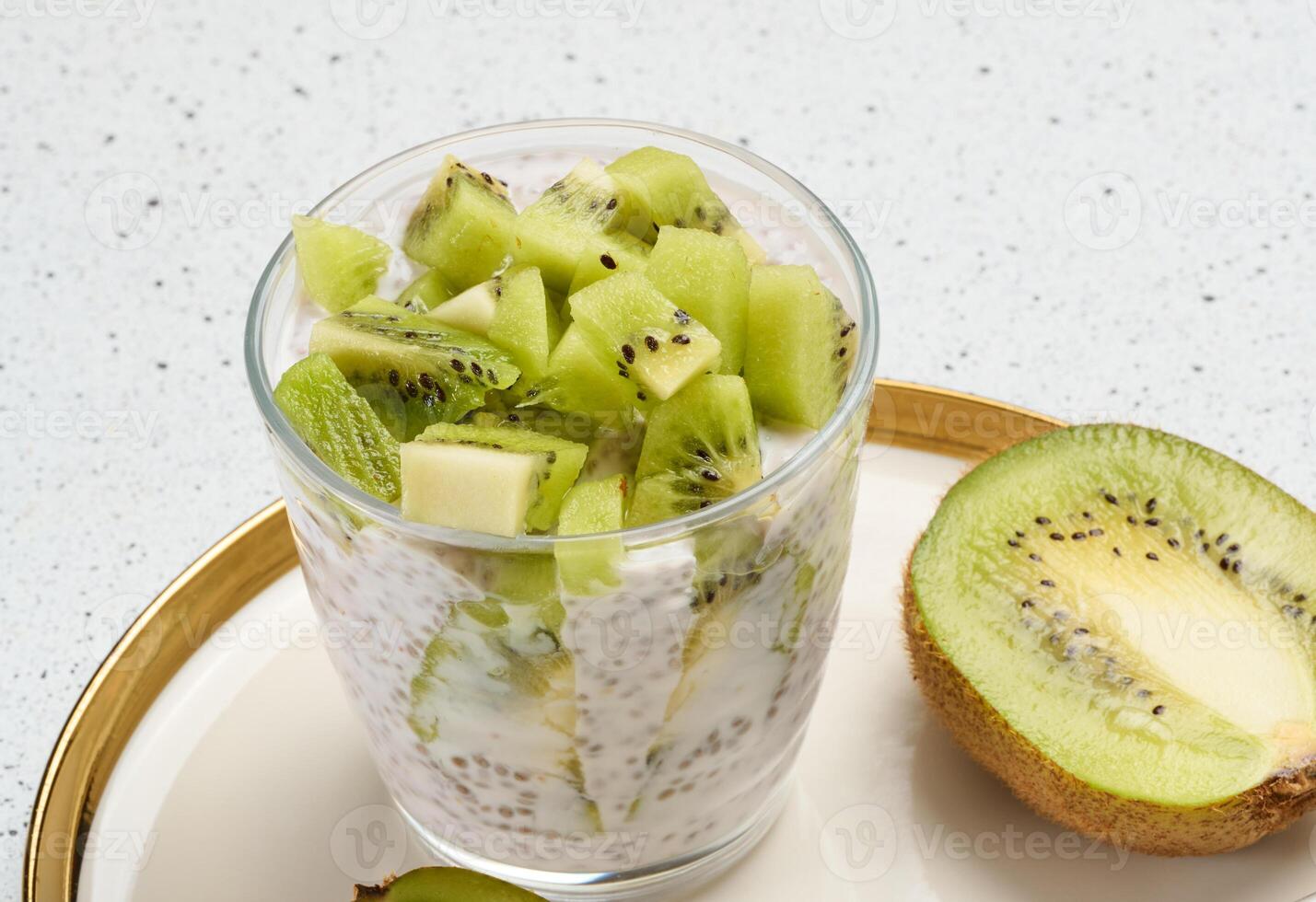 Chia seed pudding topped with diced kiwi sits on a plate with halved kiwis and a spoon. photo
