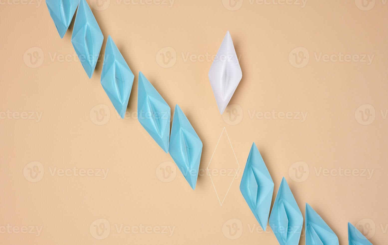 A line of blue origami paper boats with one white and the outline of the missing one, symbolizing uniqueness or a missing element photo