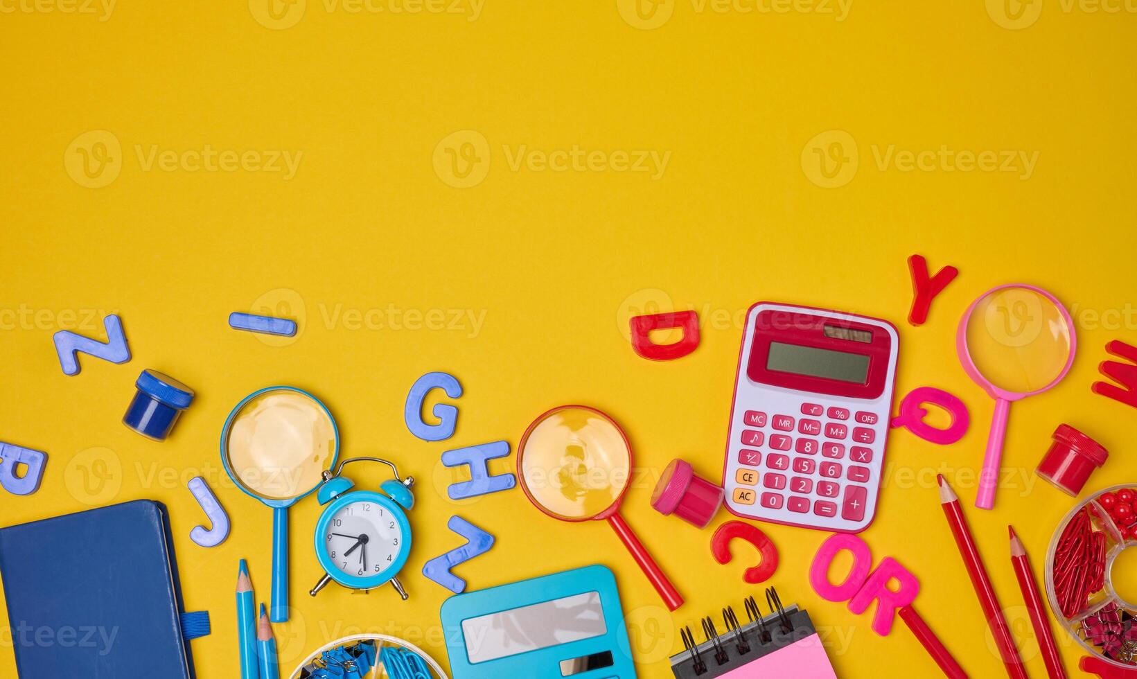 Colorful school supplies, learning items calculators, letters, tools, and stationery scattered on a vibrant yellow background. Education and back to school concept photo
