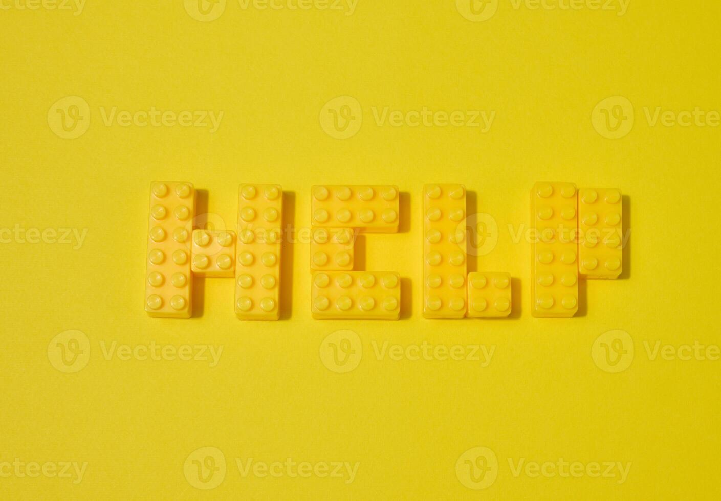 The word HELP, made from yellow toy blocks, is placed on a yellow background photo