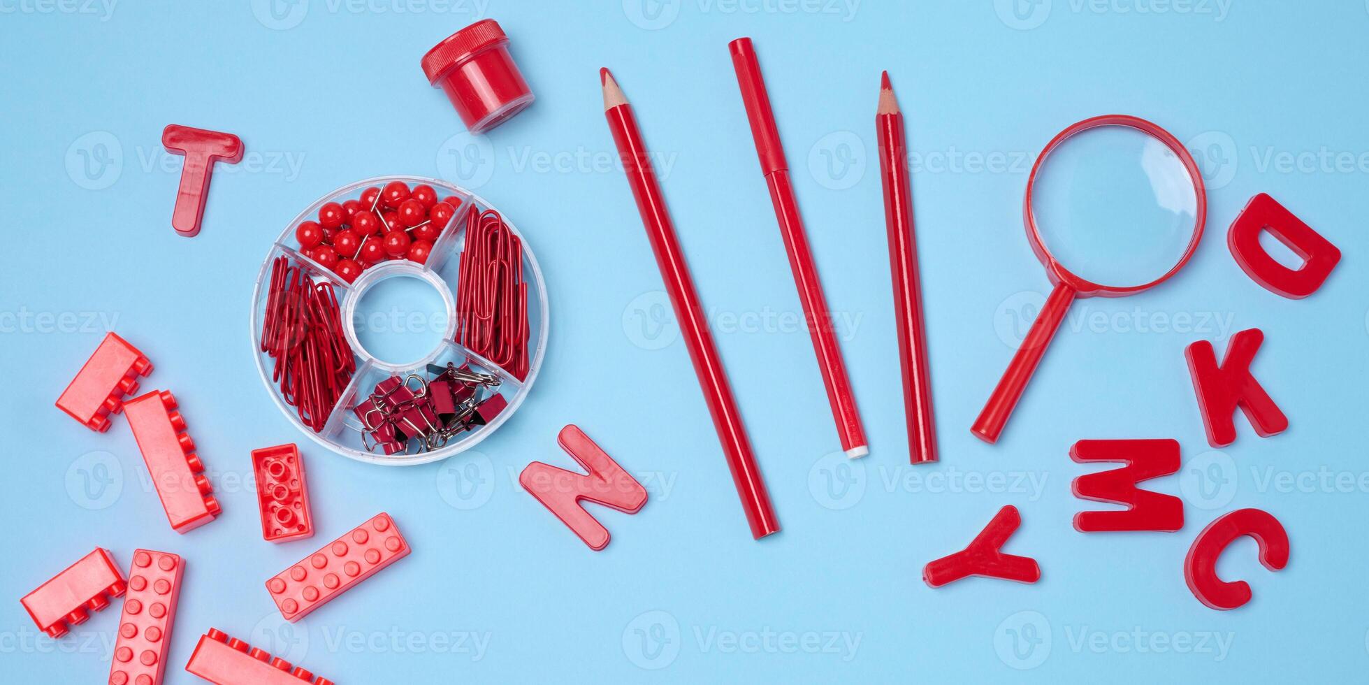 Flat lay of red stationery, learning items letters, magnifying glass, supplies, bricks, toys, and alarm clock on a light blue background. photo