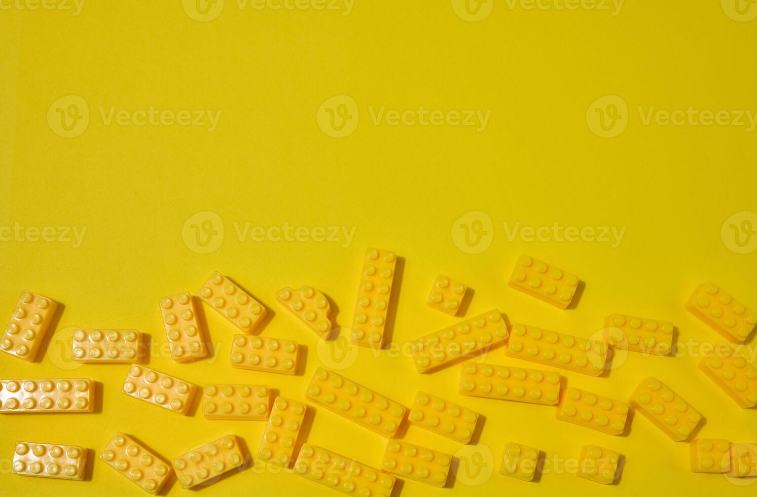 Scattered yellow plastic toy building bricks on a solid yellow background. Play, construction, education or creative concept photo