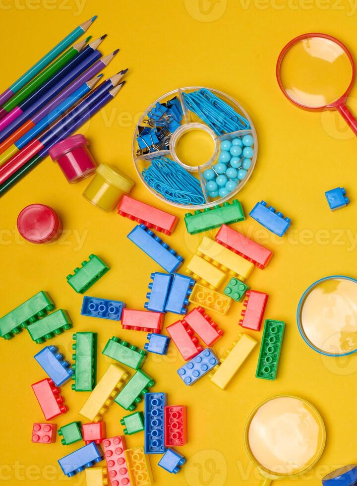 Vibrant collection of colorful school supplies, building bricks, letters, and learning items scattered on a yellow background. Play and education concept. photo