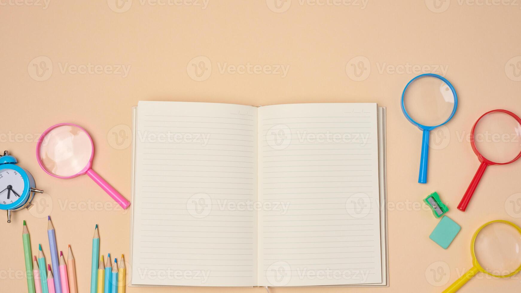 Open notebook with pastel-colored pencils, green sharpener, and turquoise eraser on a beige background. photo