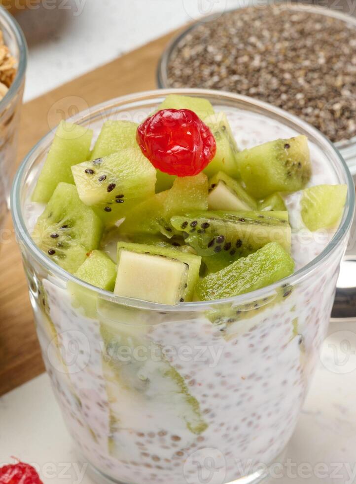 Yogurt and chia seed pudding in a glass, kiwi pieces. White table, above photo