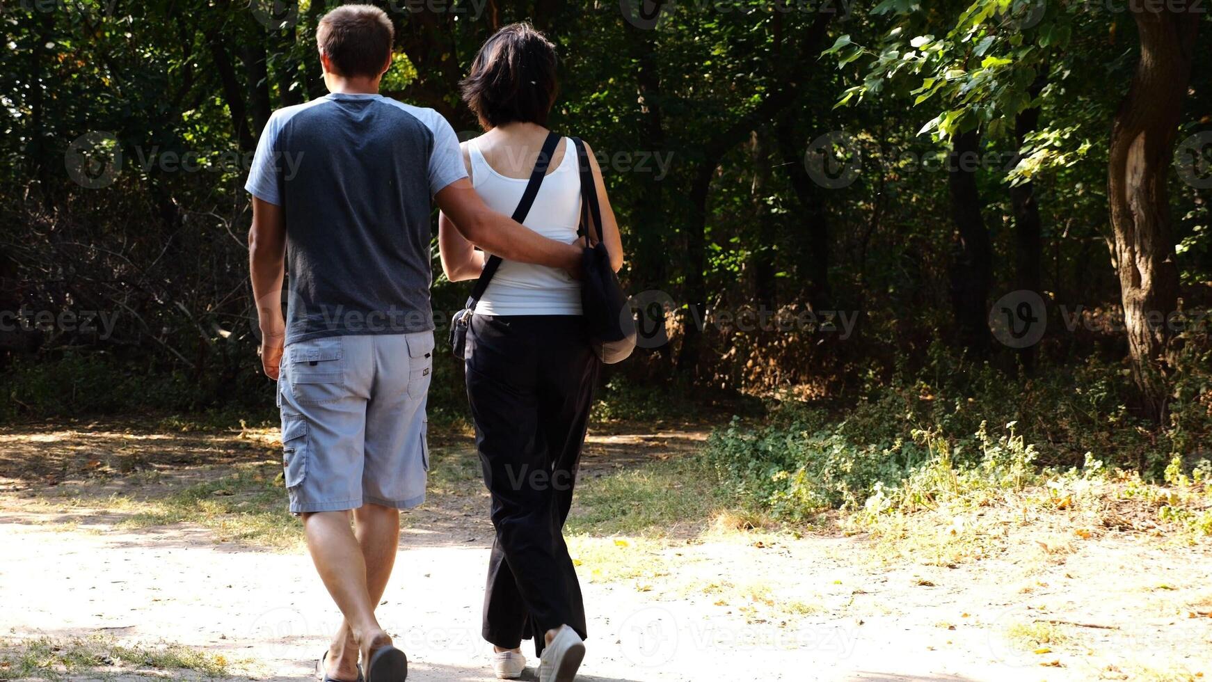Happy couple walking along path at summer forest. Romantic pair going along trail at wild woodland. Lovers spending time together at nature. Concept of love and happiness. Slow motion photo