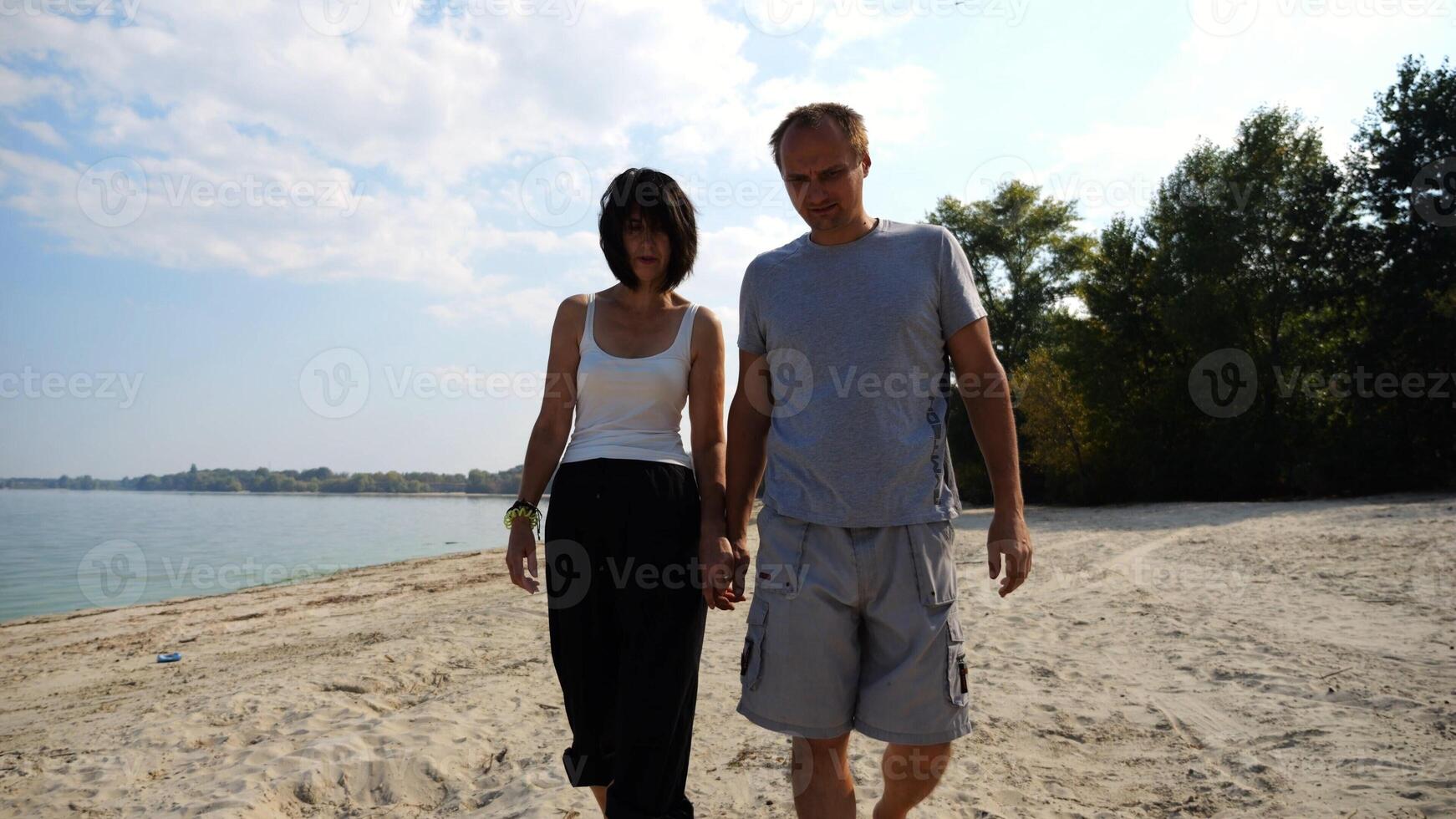 Romantic couple holding hands of each other and walking at coastline. Happy pair going along seashore at sunny day. Lovers spending time together at resort. Concept of vacation or holiday. Slow motion photo