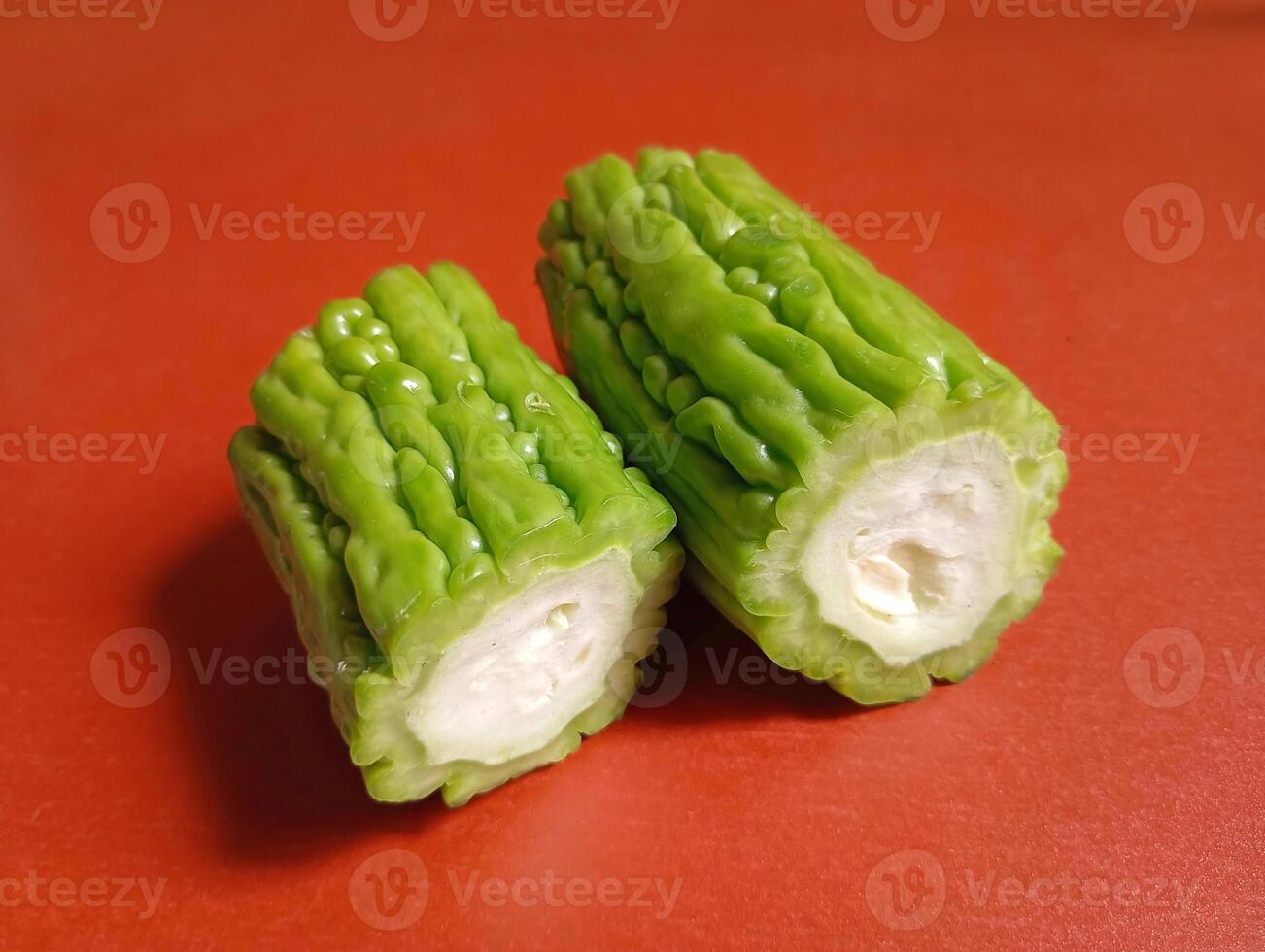 Two Green Bitter Melon Cuts. Two neatly sliced bitter melons rest on a red surface, highlighting their wrinkled skin and firm interior. photo