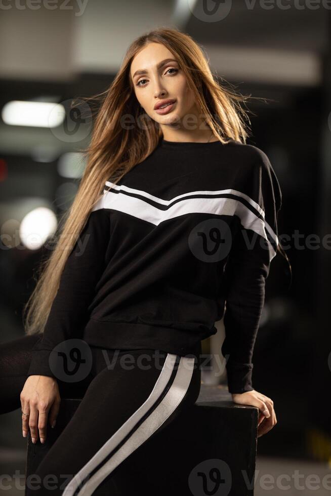 fitness enthusiast presents stylish athletic wear while seated on bench in modern gym. Bright lights enhance mood of wellness and health photo
