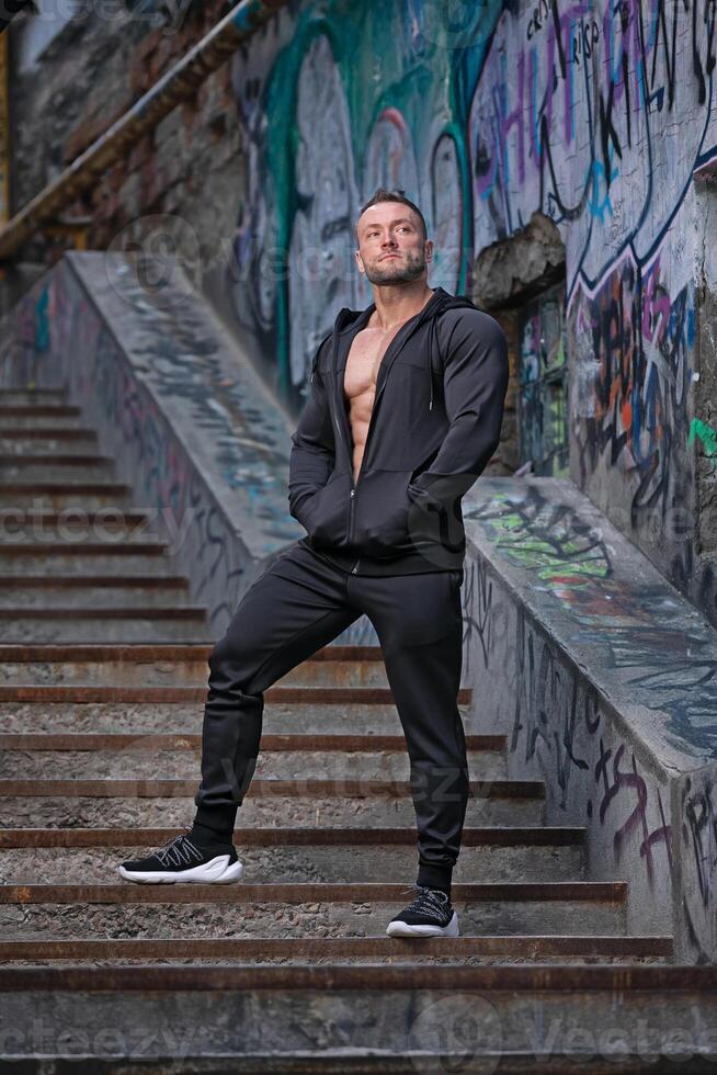 Strong male model poses confidently on urban stairs with colorful graffiti background photo