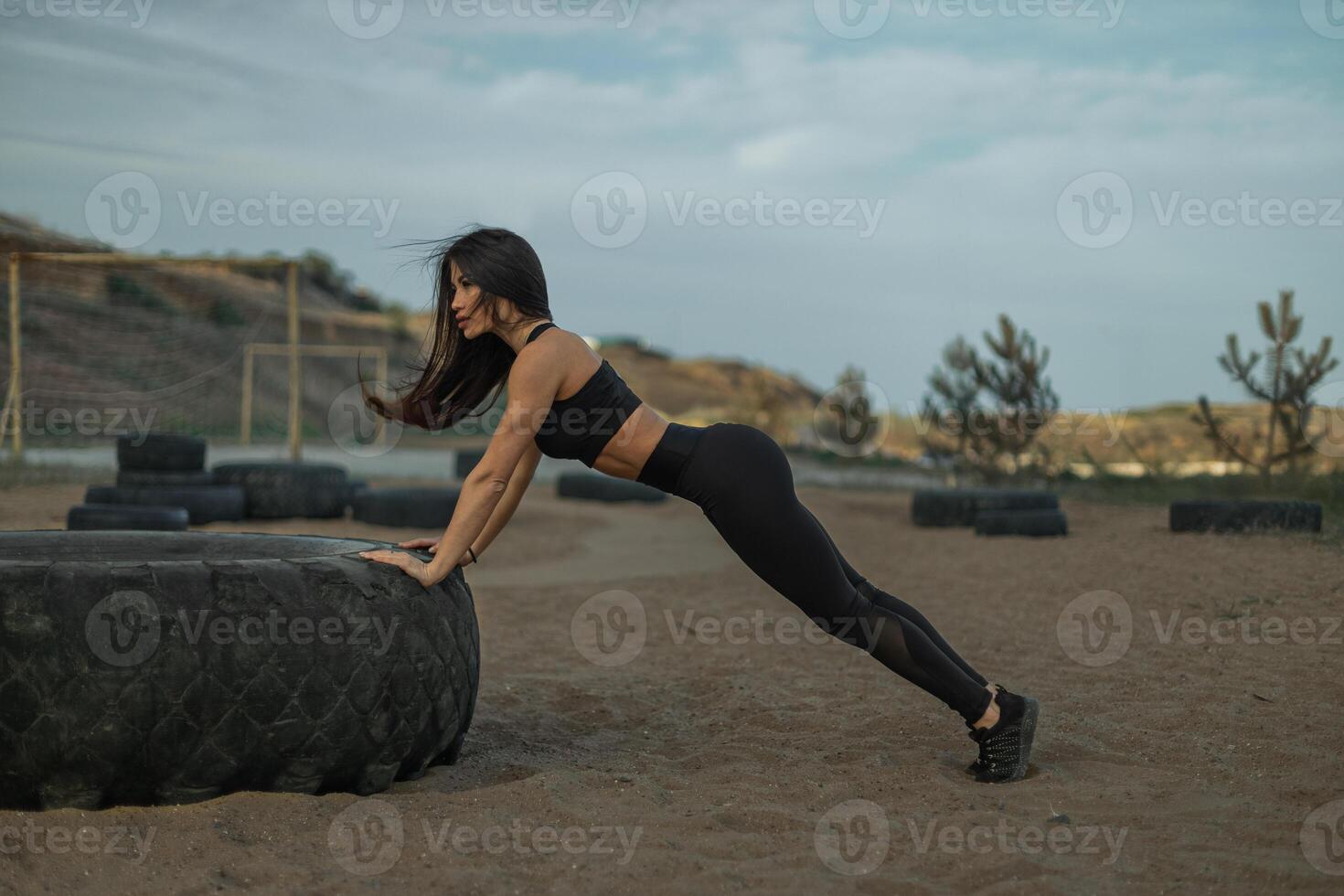 Woman performs push ups on large tire in outdoor gym setting during daytime workout photo