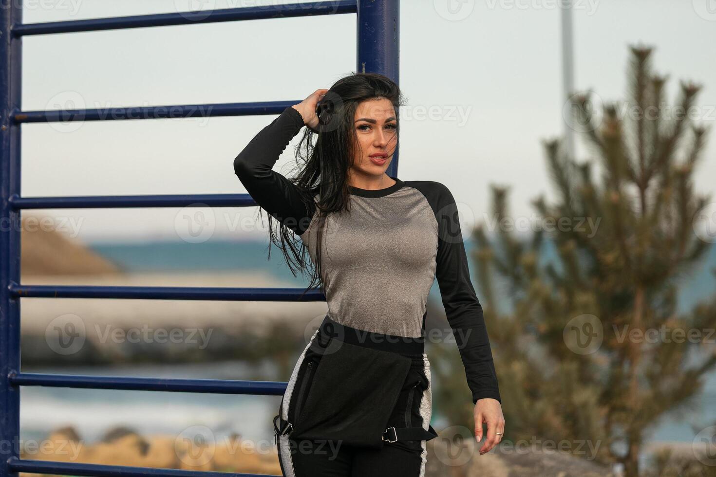 Fitness enthusiast posing near a seaside park at sunset with workout attire and a playful expression photo