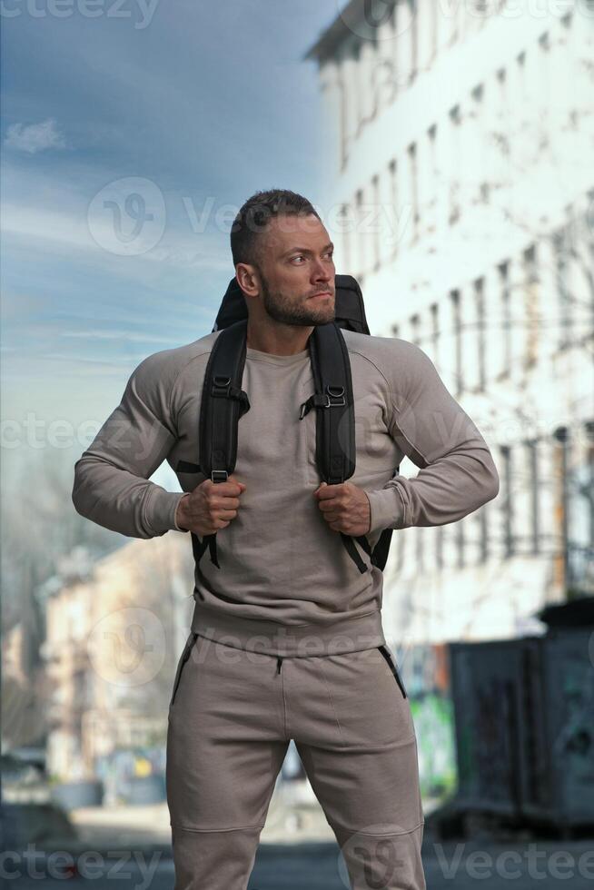 Muscular man in urban setting with backpack demonstrates strength and readiness for adventure photo