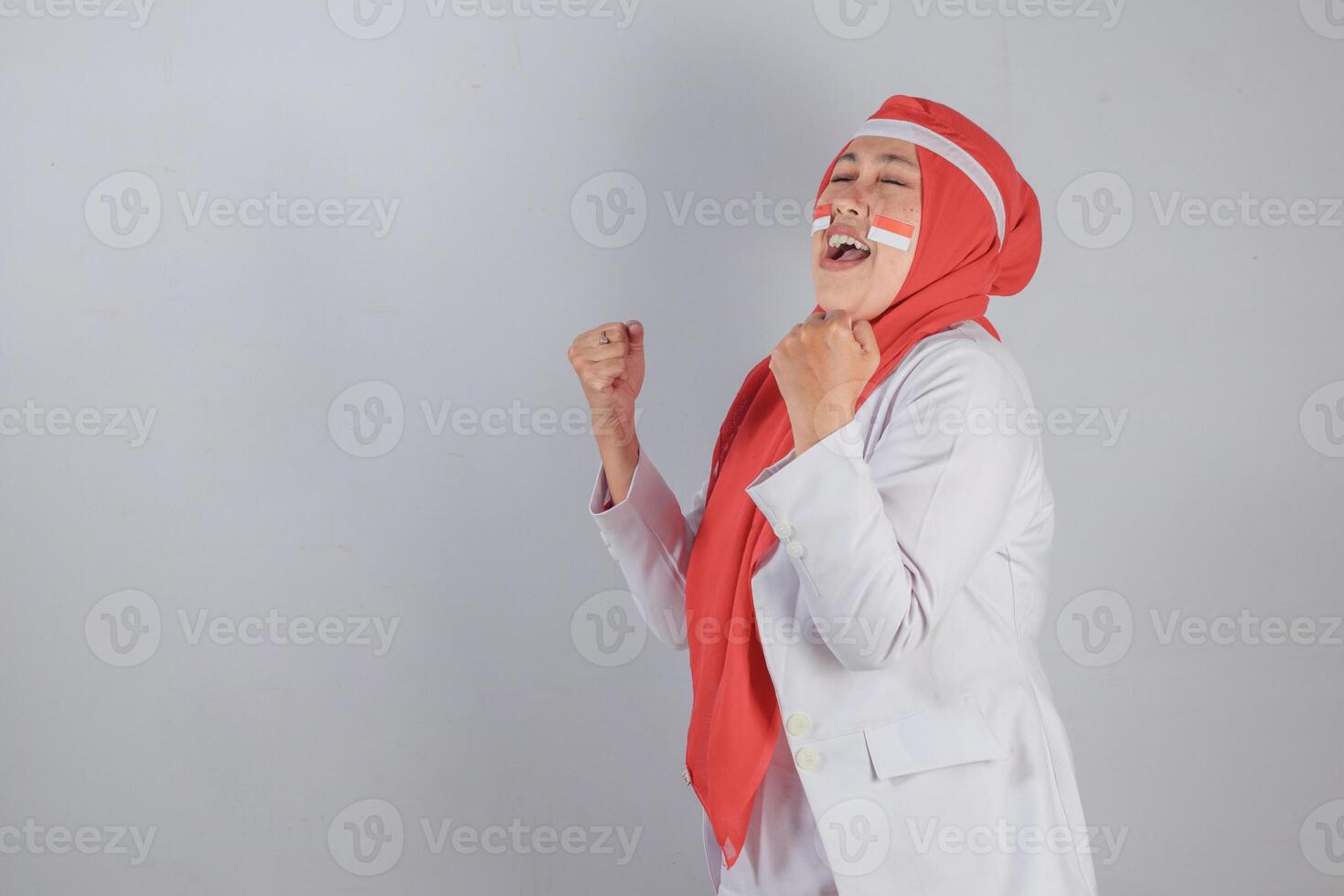 Joyful Indonesian woman celebrating with clenched fists and patriotic face paint expressing national pride and energetic triumph emotion in victory pose perfect for themes of motivation and unity photo