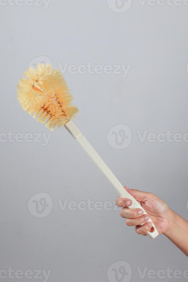 Hand gripping toilet brush with yellow bristles and white handle in diagonal position photo