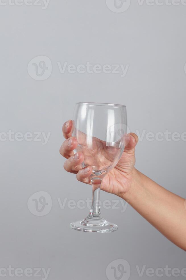 Human hand firmly holding empty wine glass by the stem with fingers wrapped around clear glassware isolated on neutral background for hospitality or celebration concept photo