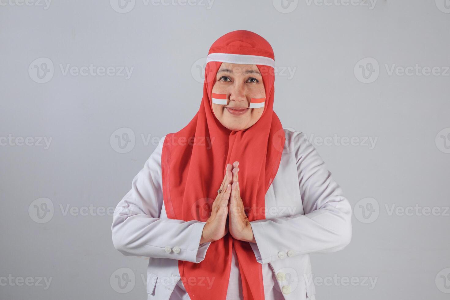 Portrait of mature Southeast Asian Muslim woman with face paint doing respectful greeting gesture to show patriotism and cultural pride during national celebration photo