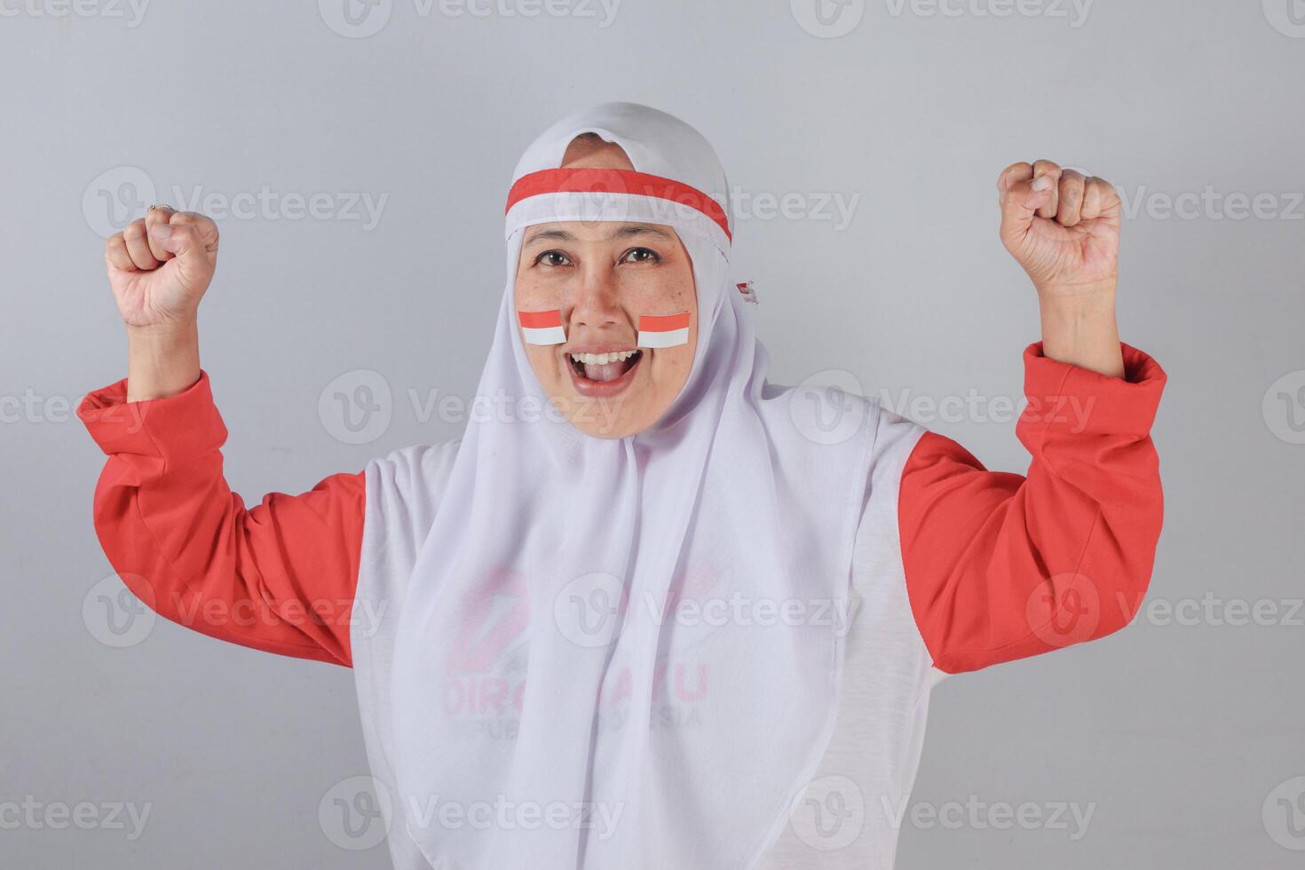Indonesian woman in hijab with flag face paint celebrating with fists raised and smiling photo