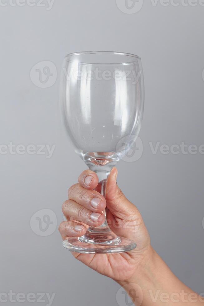 Hand holding empty wine glass by the base with fingers wrapped around clear transparent stemware for drinking or celebration themes on neutral background photo
