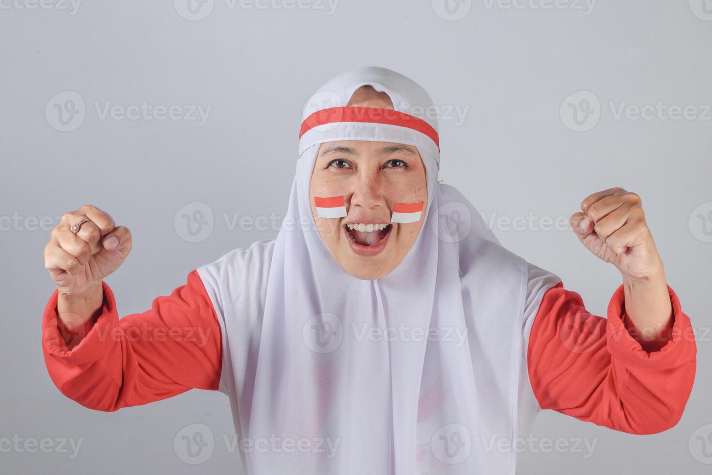 Indonesian woman in hijab with flag face paint clenching fists and shouting with joy photo