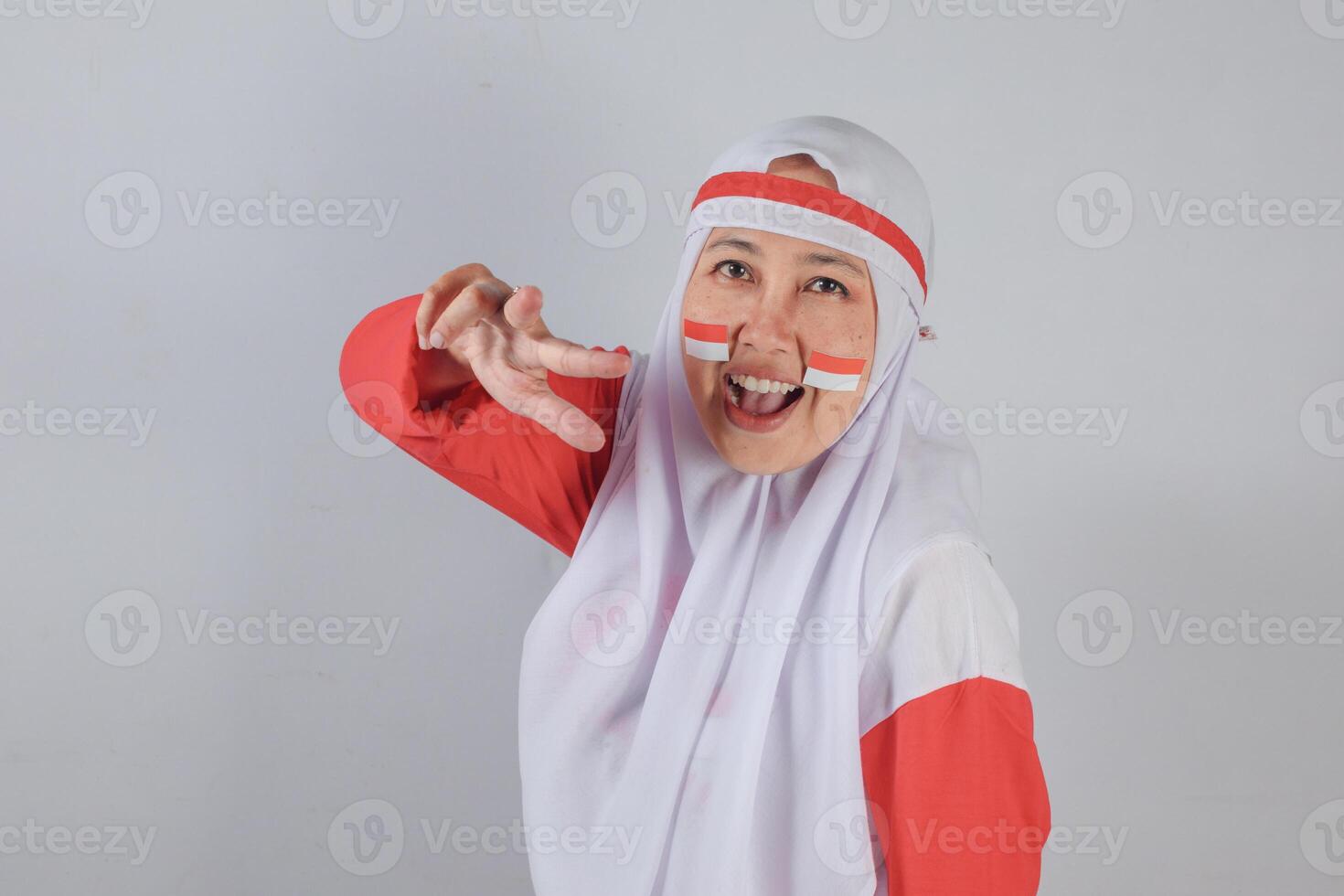 Cheerful Muslim woman in hijab with Indonesian flag face paint making peace sign while smiling joyfully, expressing national pride, happiness, and youthful celebration photo