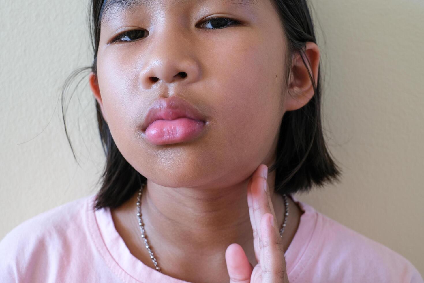 Portrait of Asian young girl has chin pain, kid painful use finger touching itching her chin. Health and medical problem and Dental care concept. Lymphadenitis chin problem. swollen lymph nodes. photo