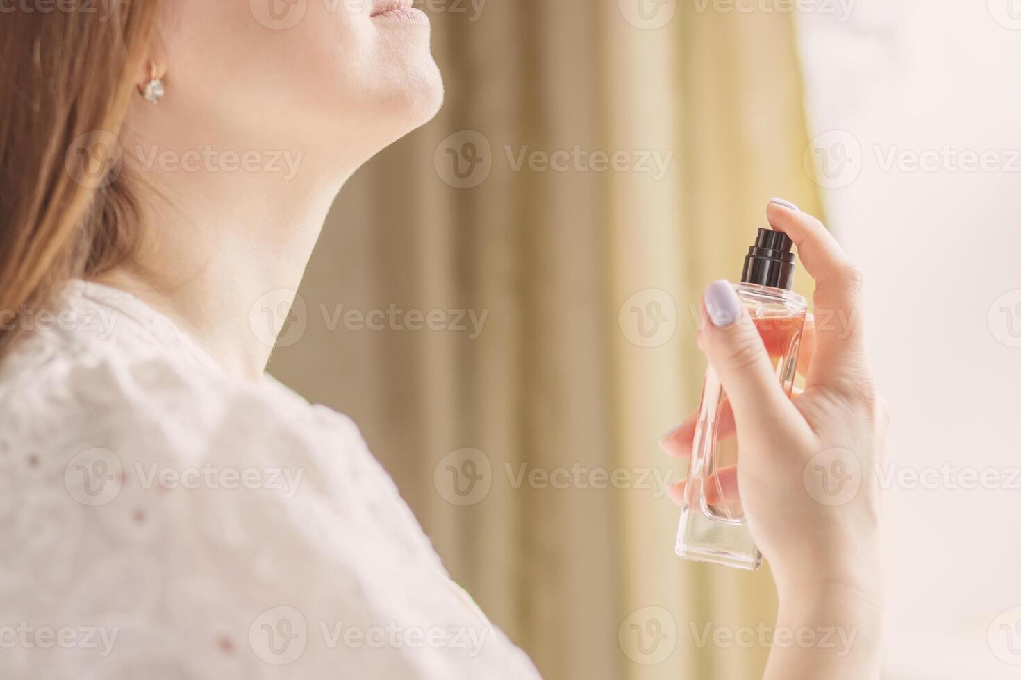 Beautiful young woman holds bottle of perfume and spraying it on neck photo