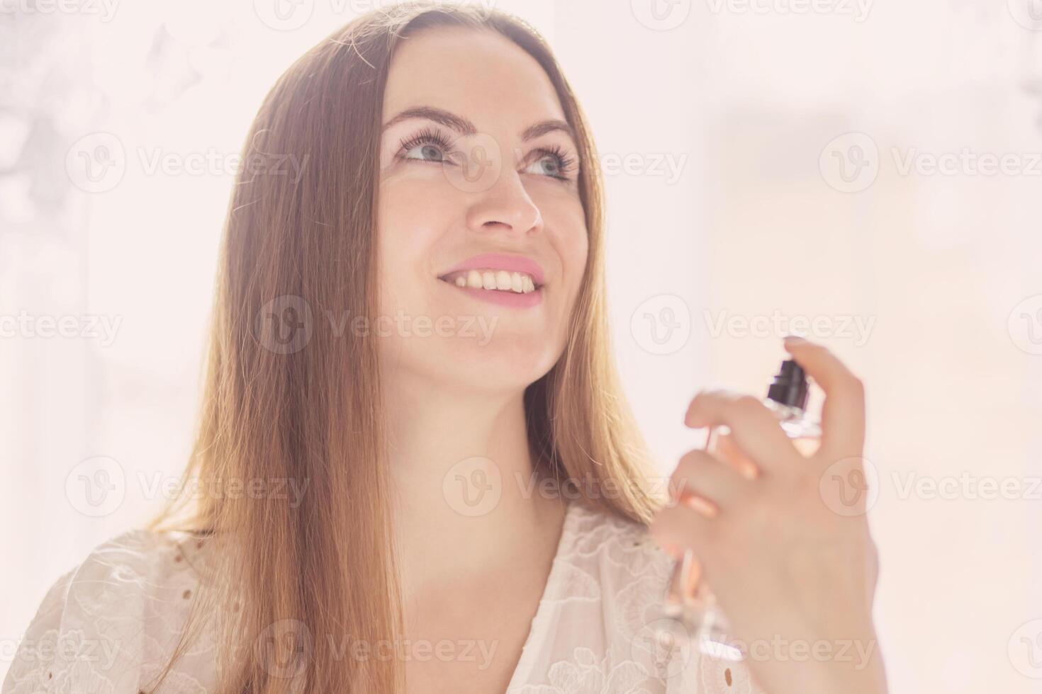 Beautiful young woman holding a bottle of perfume and applying it photo