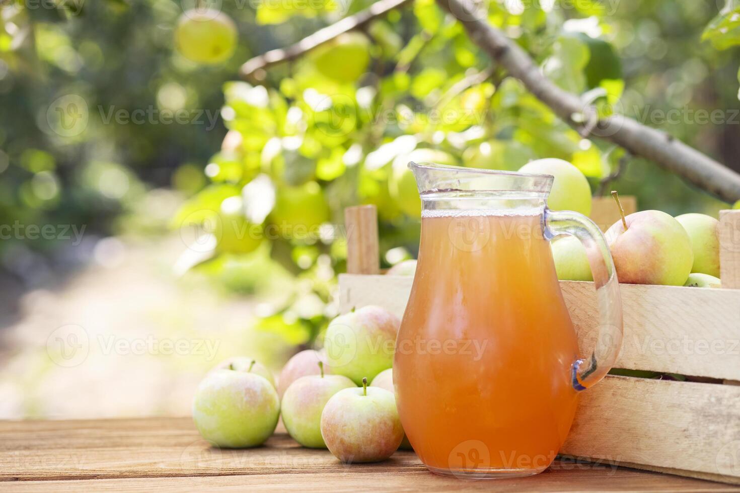 Apples, box of apples and pitcher of fresh apple juice on wooden table with garden background. Harvest of apples. Juice production photo