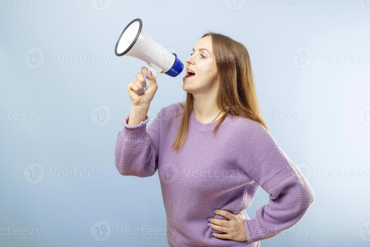 Young brunette woman shouting loudly while holding megaphone on blue background photo