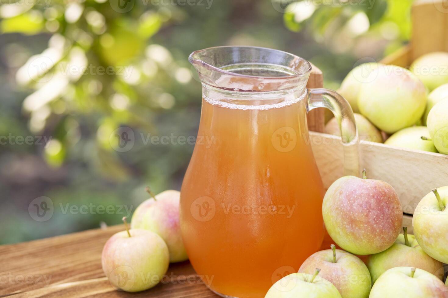 Apples, box of apples and pitcher of fresh apple juice on wooden table photo