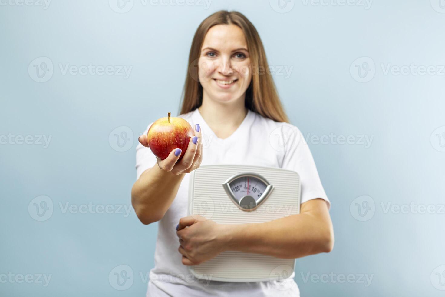 Happy smiling woman holding weight scales and red apple on a blue background photo