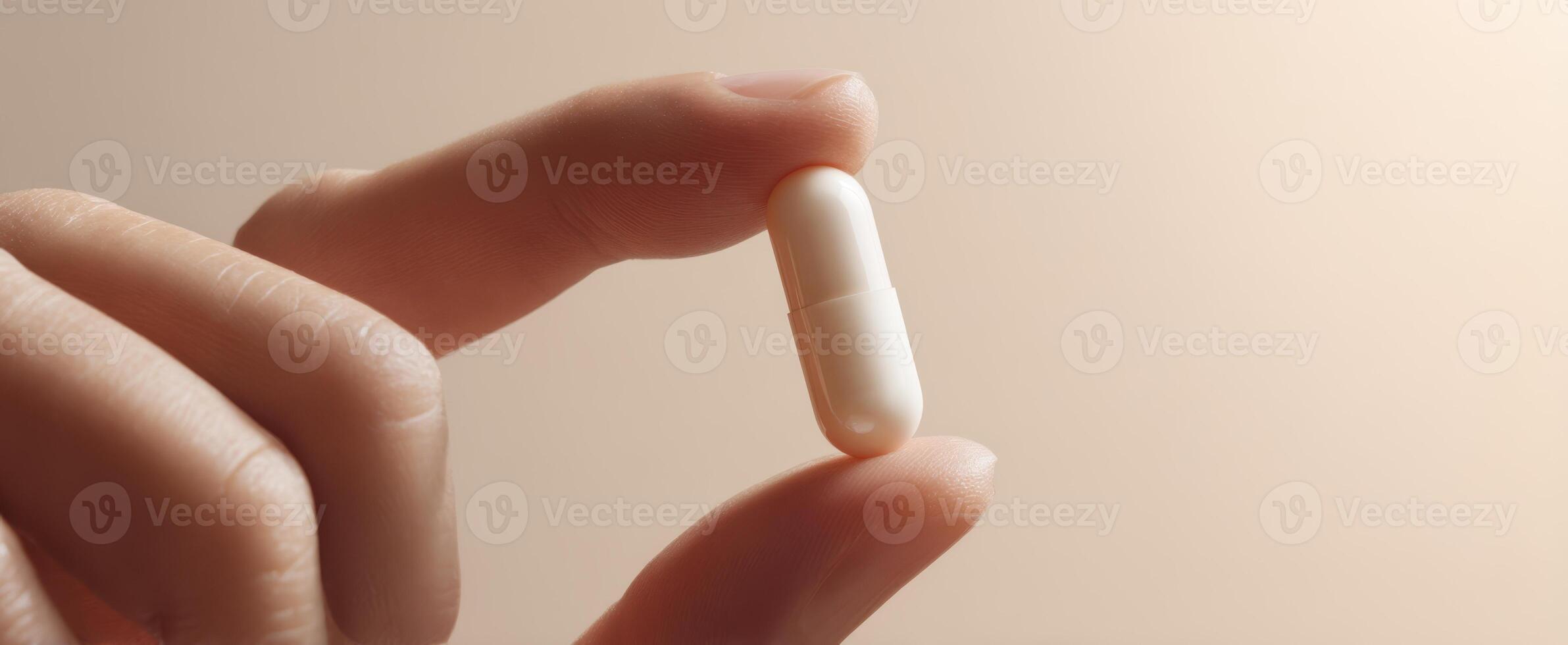 The hand gently holds a white capsule in soft light settings. photo