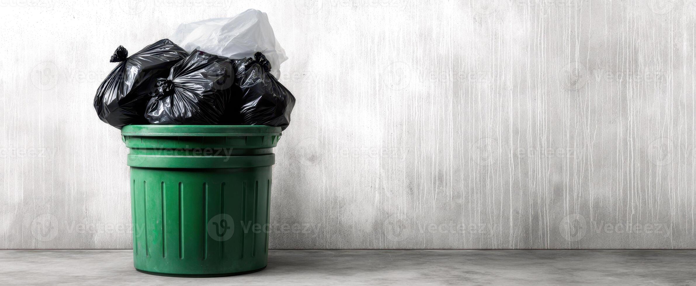 The green trash bin overflowing with black garbage bags on a concrete background photo