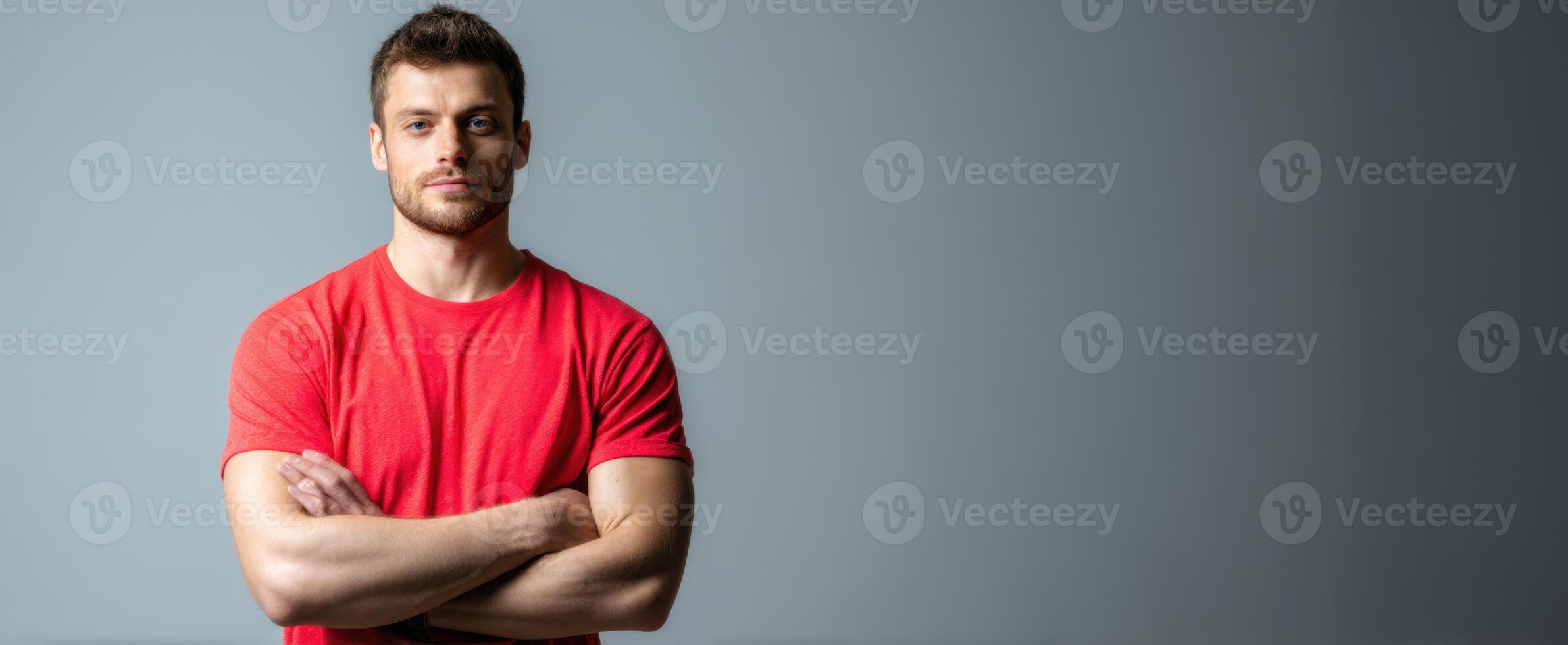 The confident man standing with arms crossed wearing a red shirt in studio setting. photo