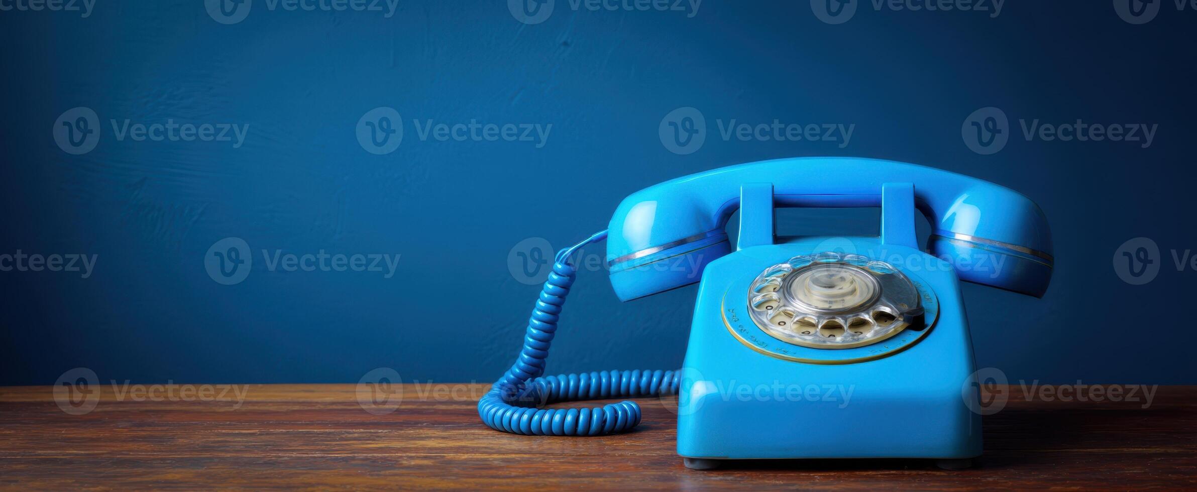 The blue rotary phone resting on a wooden table against a deep wall. photo