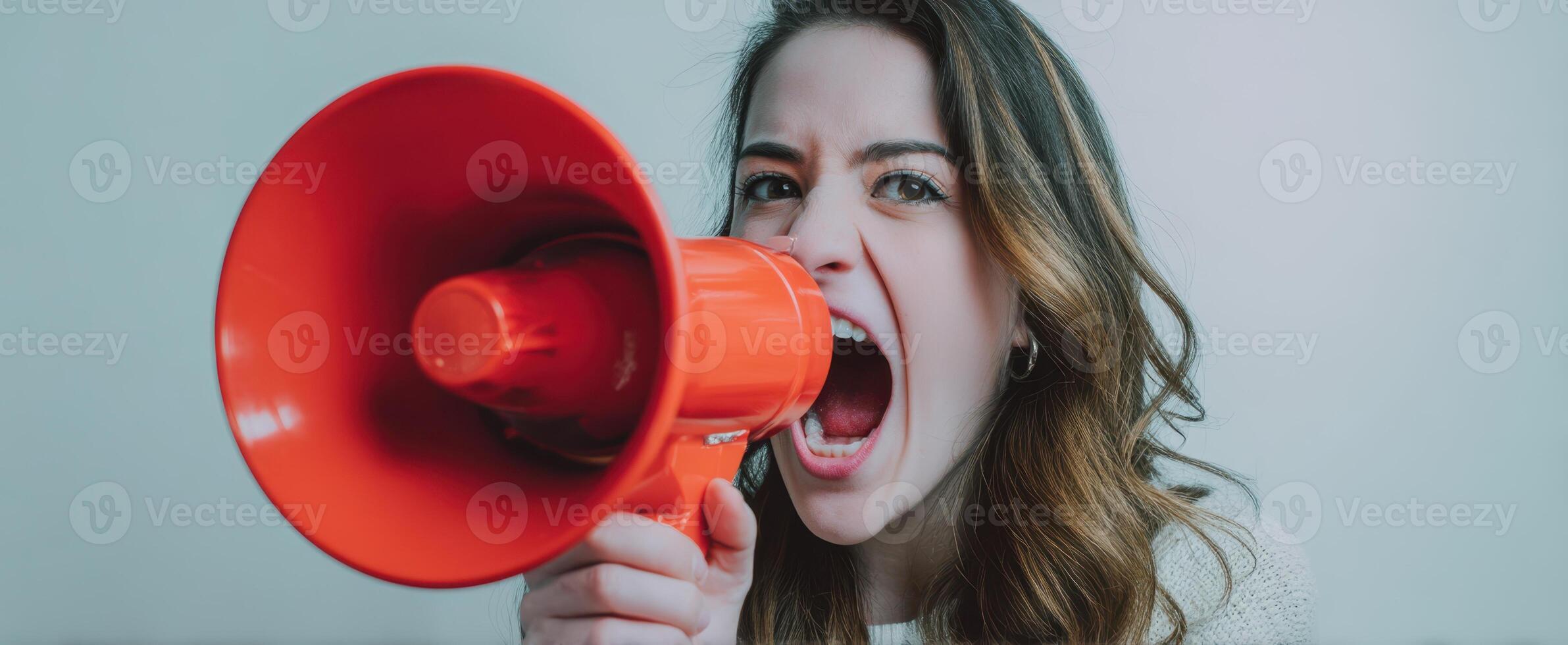 The woman passionately shouting into a bright orange megaphone in a studio setting. photo