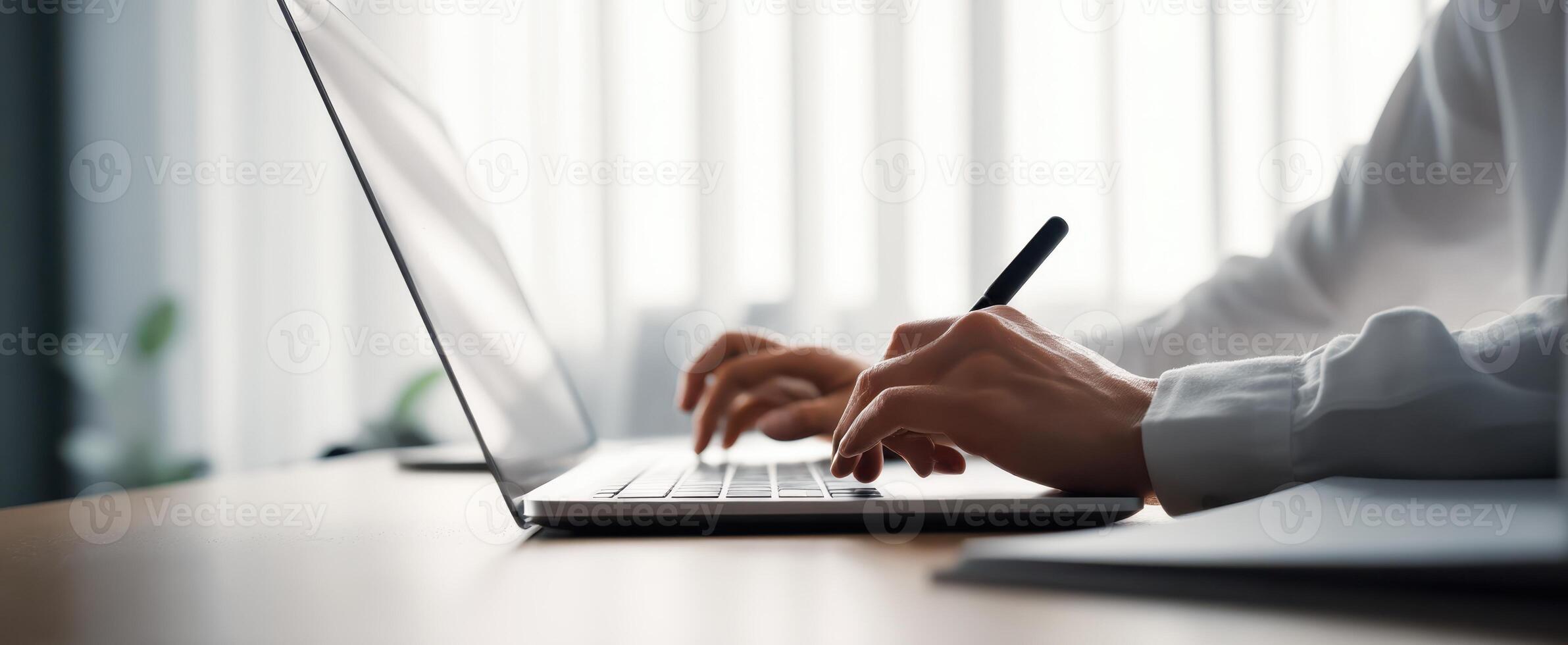 The focused individual typing on a laptop with a pen in hand photo