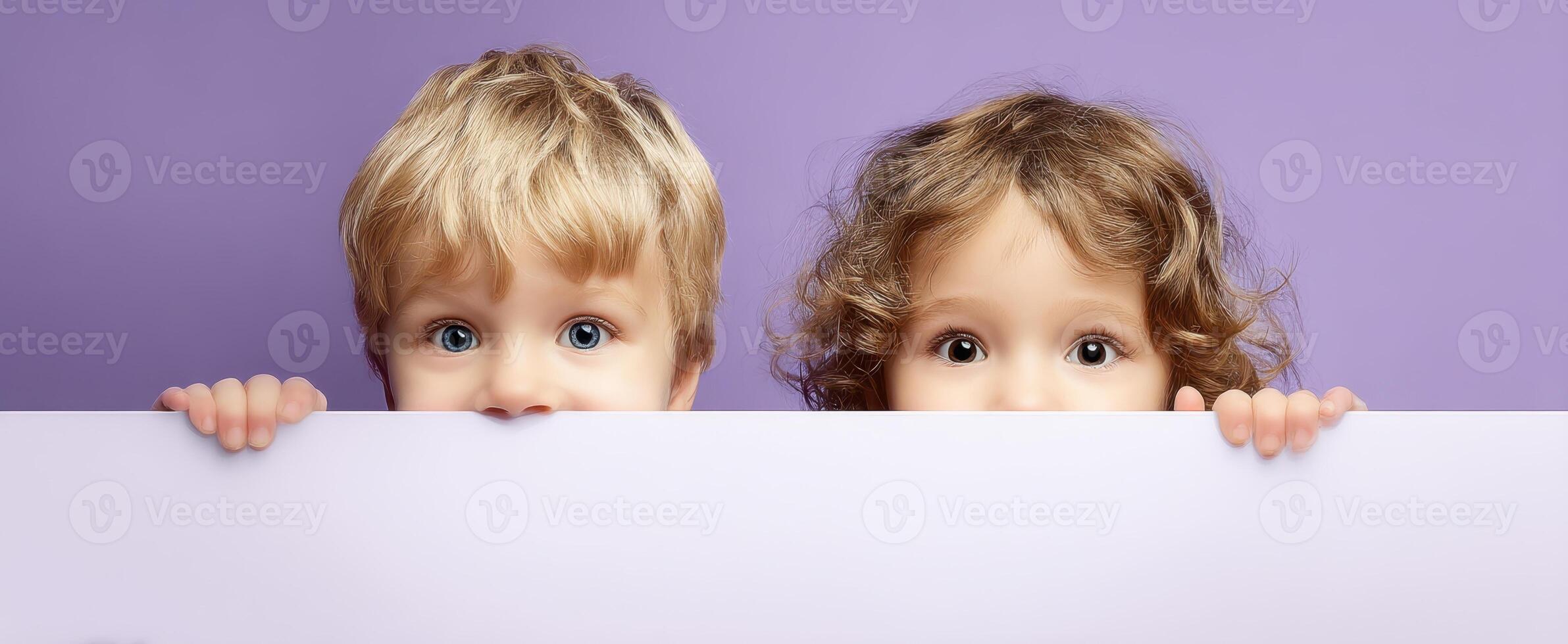 The curious children peeking over a pastel backdrop with bright expressions. photo