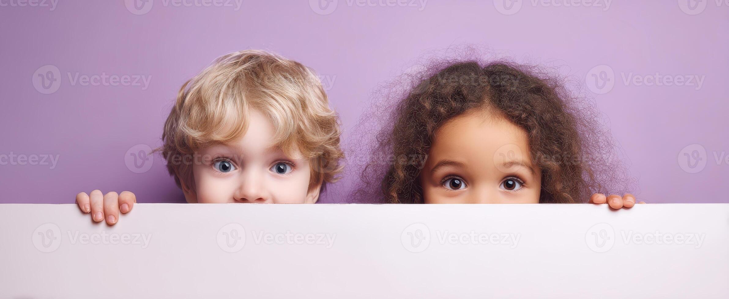 The adorable children peeking over a blank space with joyful expressions. photo