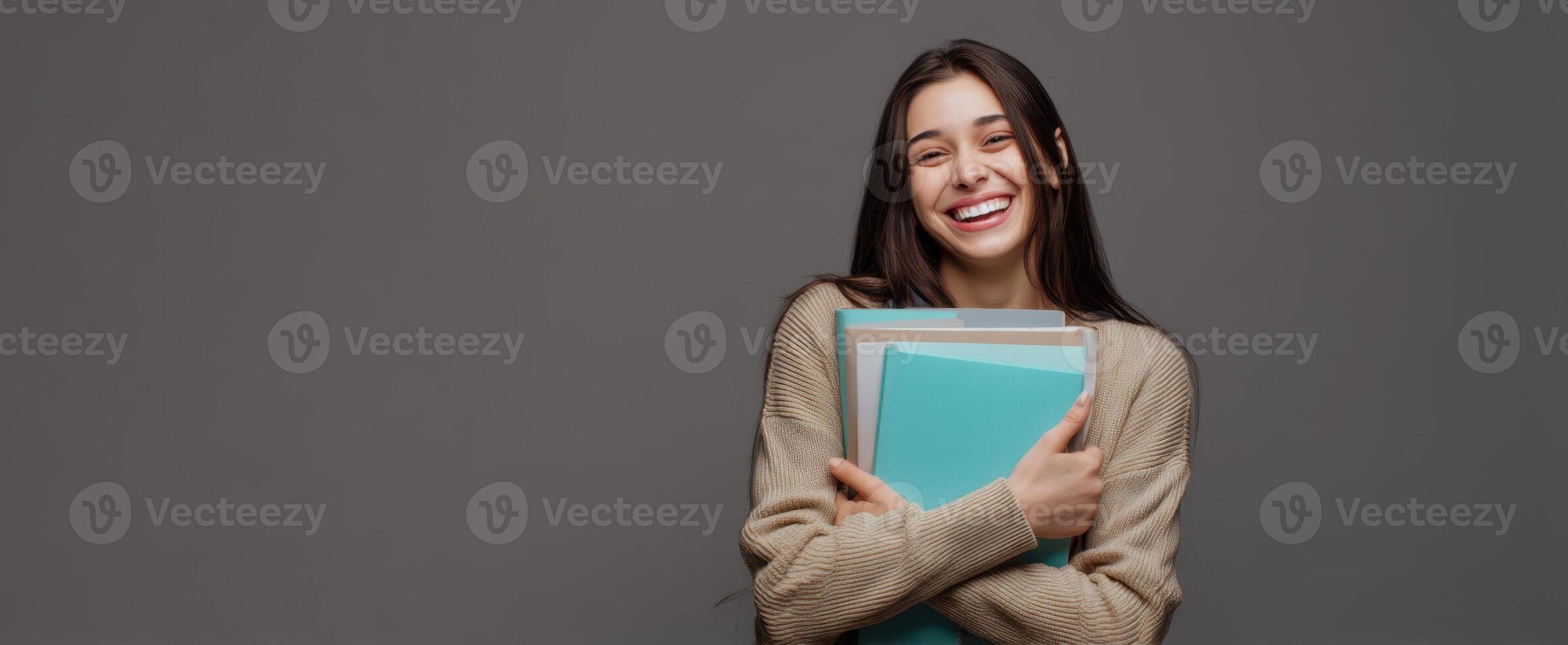 The cheerful student embraces her books with a joyful smile against a gray background. photo