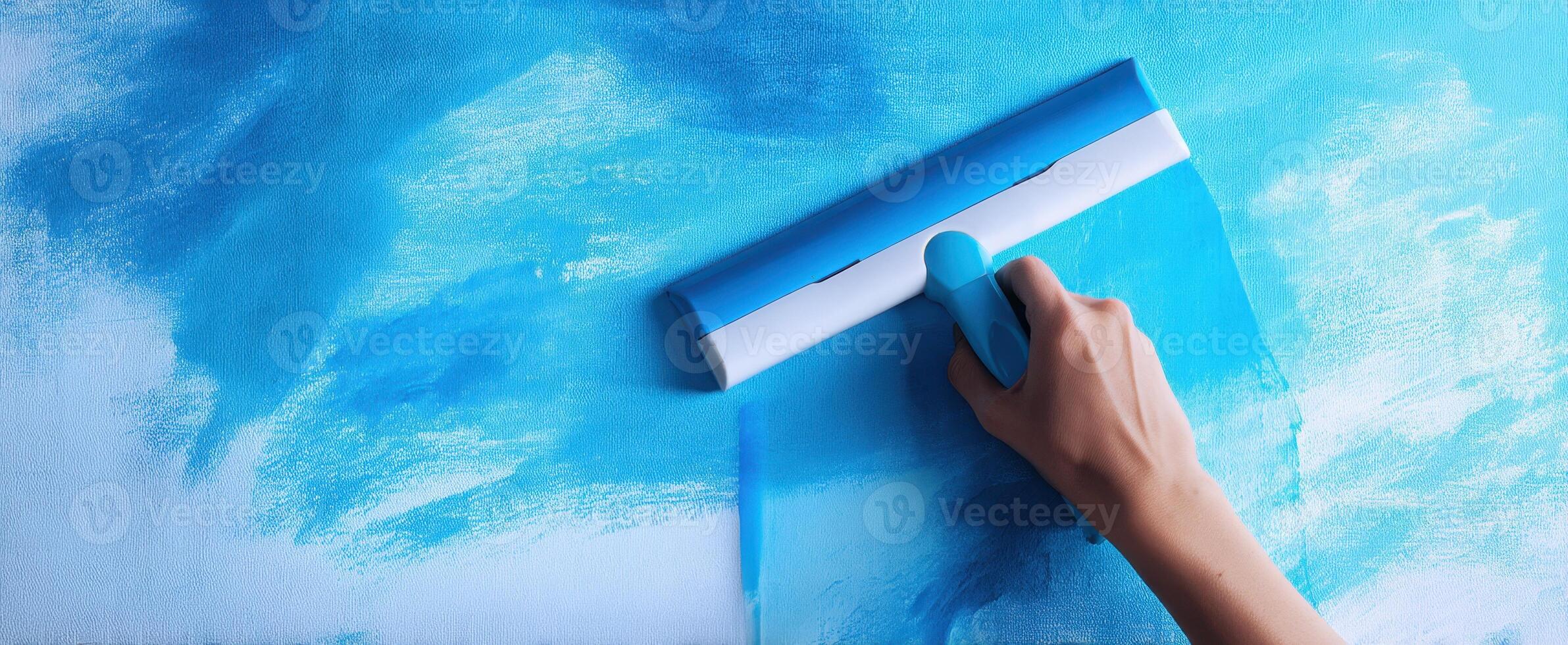 The person painting a blue canvas with a roller tool in a creative space. photo