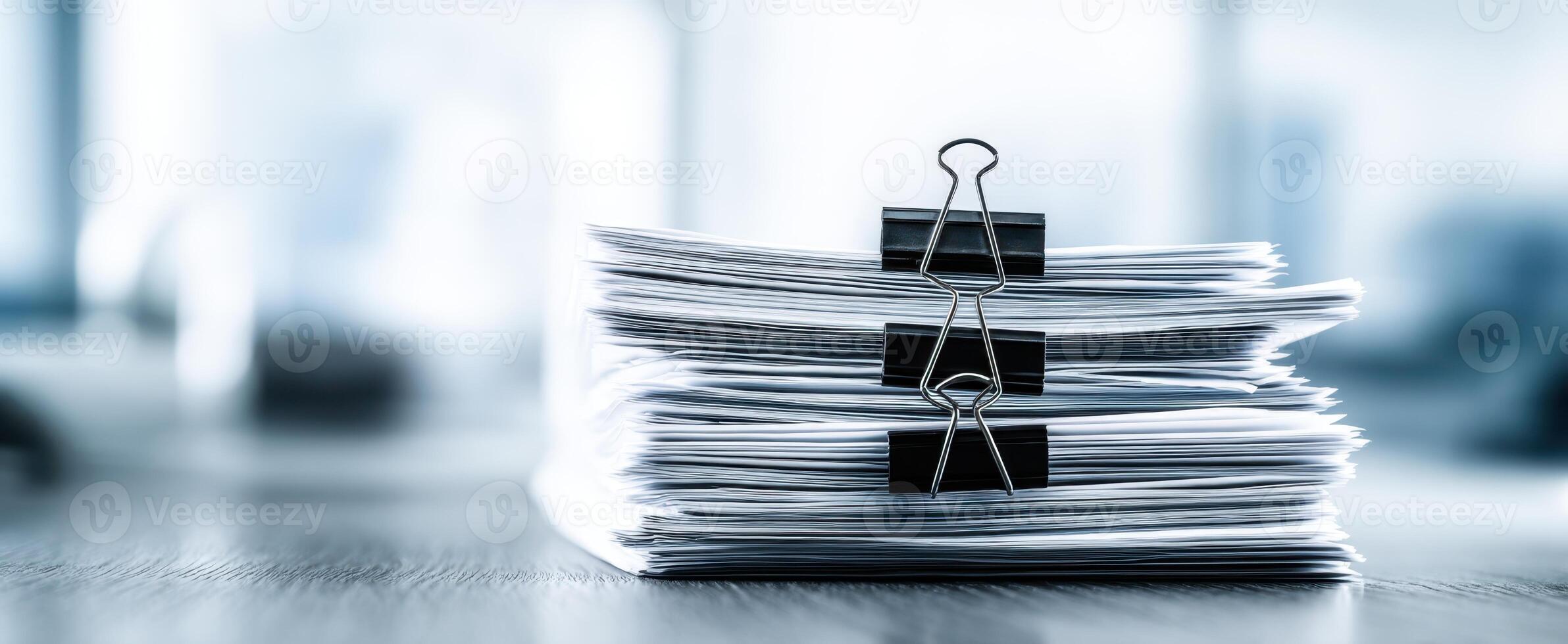 The stack of documents secured with binder clips resting on a wooden desk. photo