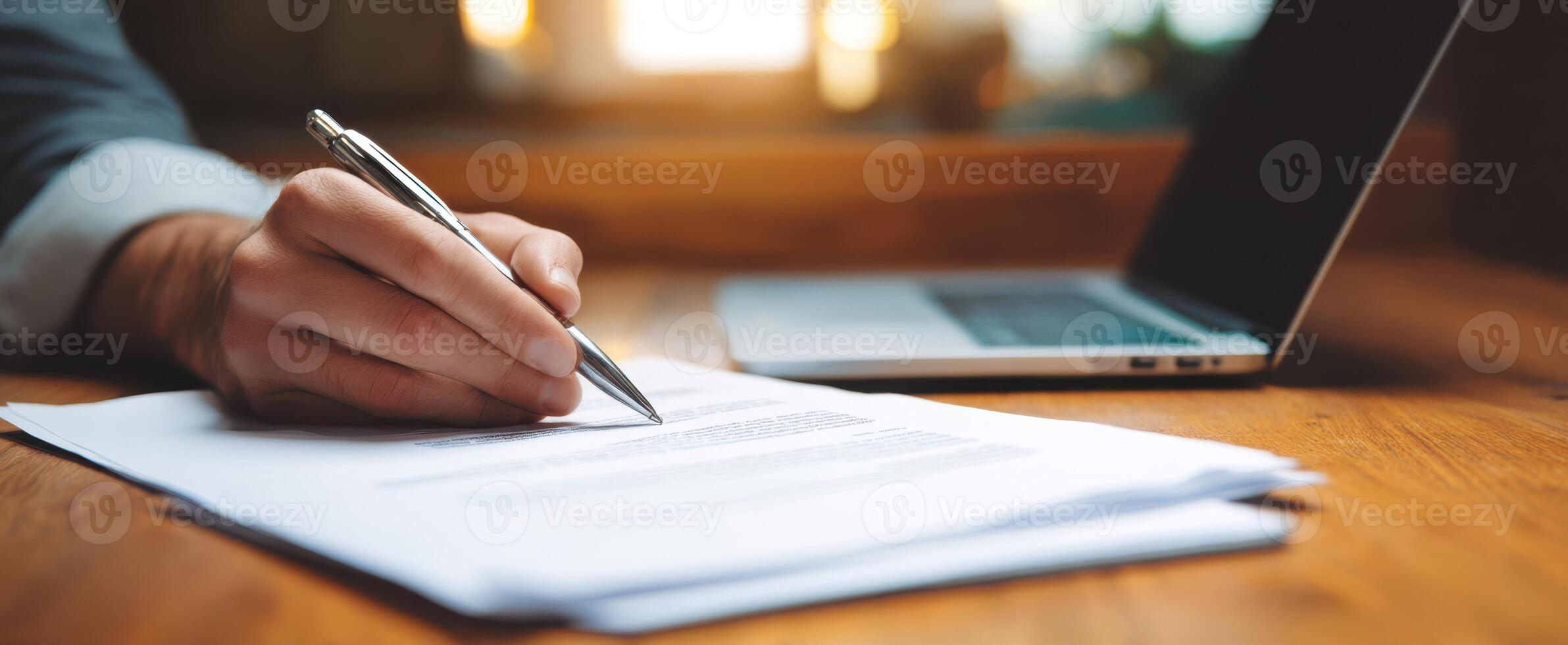 The Hand Writing on Documents Next to a Laptop in a Cozy Workspace photo