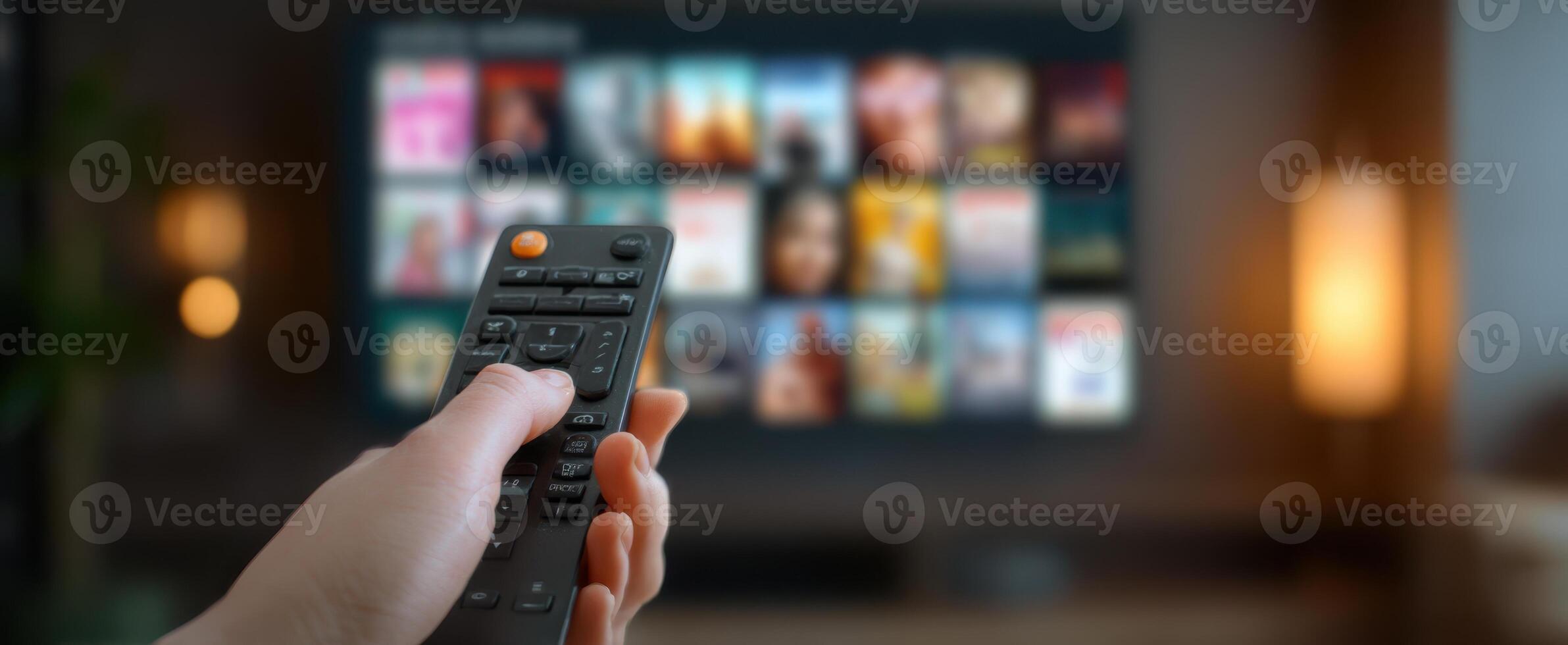 The remote control in hand with a vibrant TV streaming selection in the background. photo