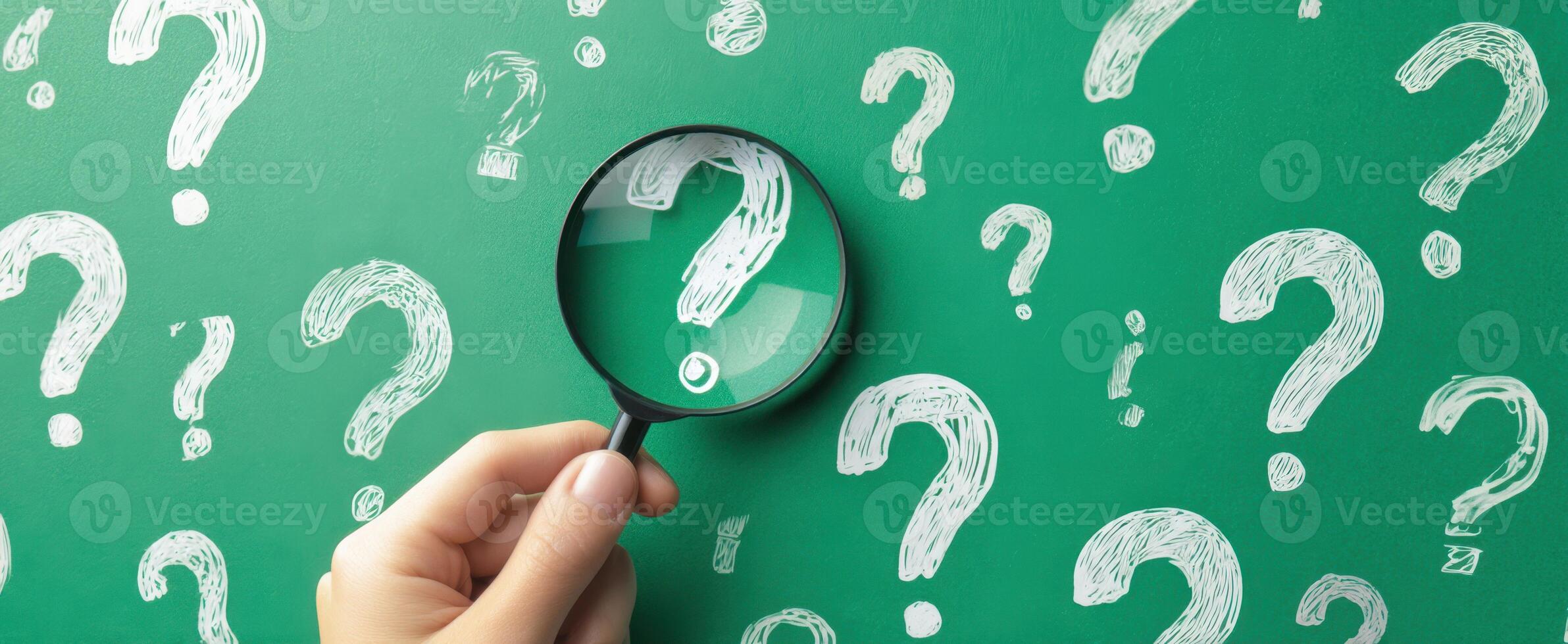 The Hand Holding a Magnifying Glass Over Question Marks on a Chalkboard Background photo