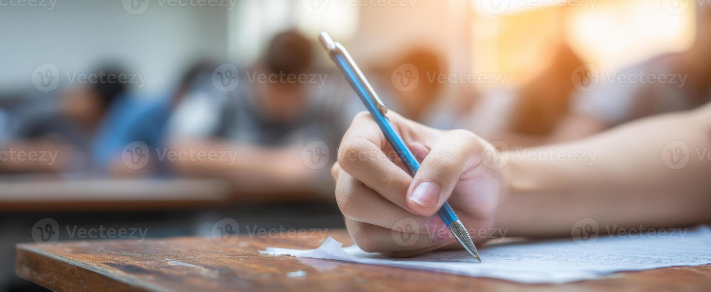 The student writing during an exam in a busy classroom environment. photo