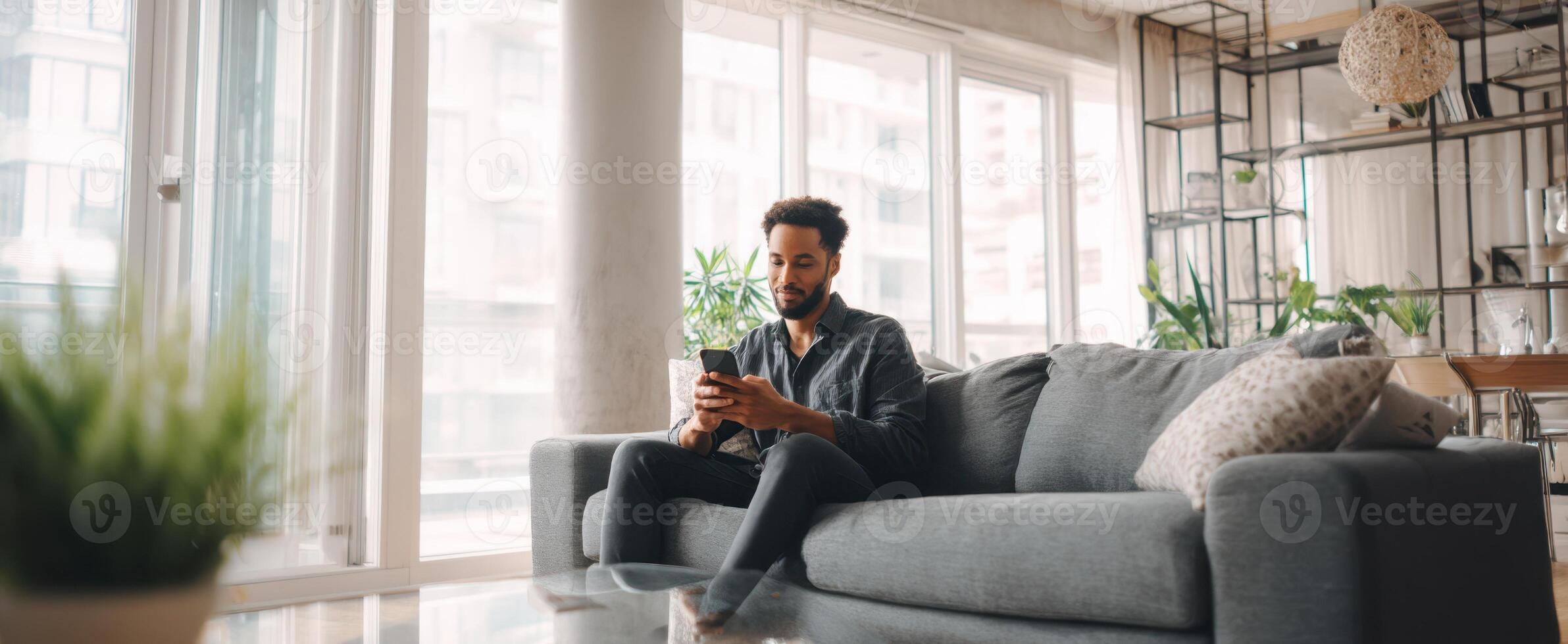 The man sitting comfortably on a couch using his smartphone in a modern apartment. photo